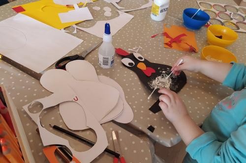 KIBIZ Schwörstadt Ein Kind bastelt mit Kleber und Schere aus Papier ein schwarzes Huhn.